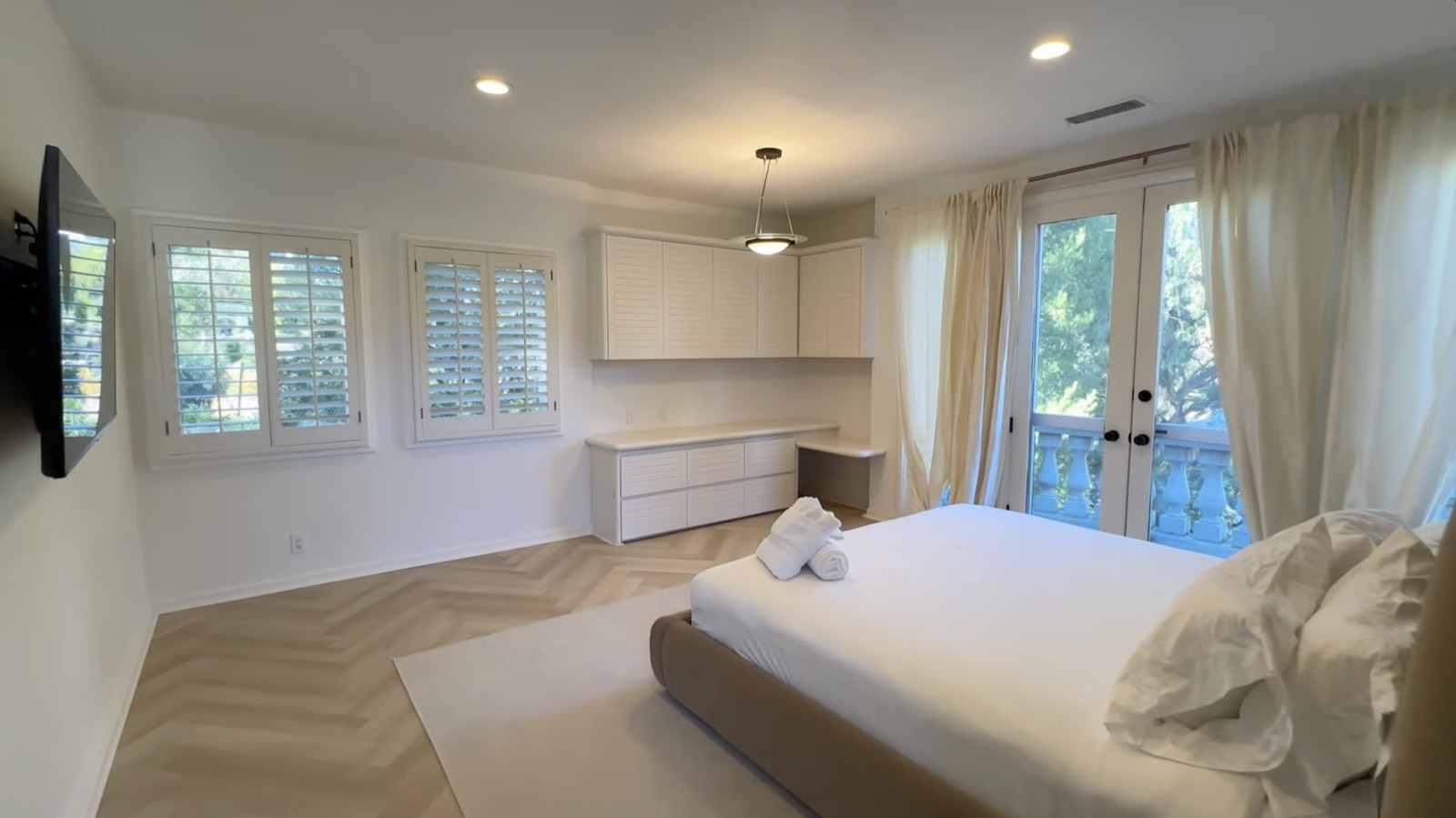 A light-filled private bedroom with plantation shutters and French doors to a balcony