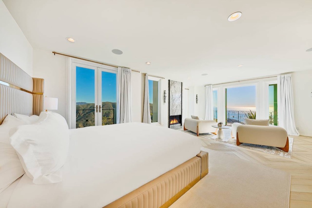 The master suite: a king bed, marble fireplace, sitting area, and the ocean beyond the balcony