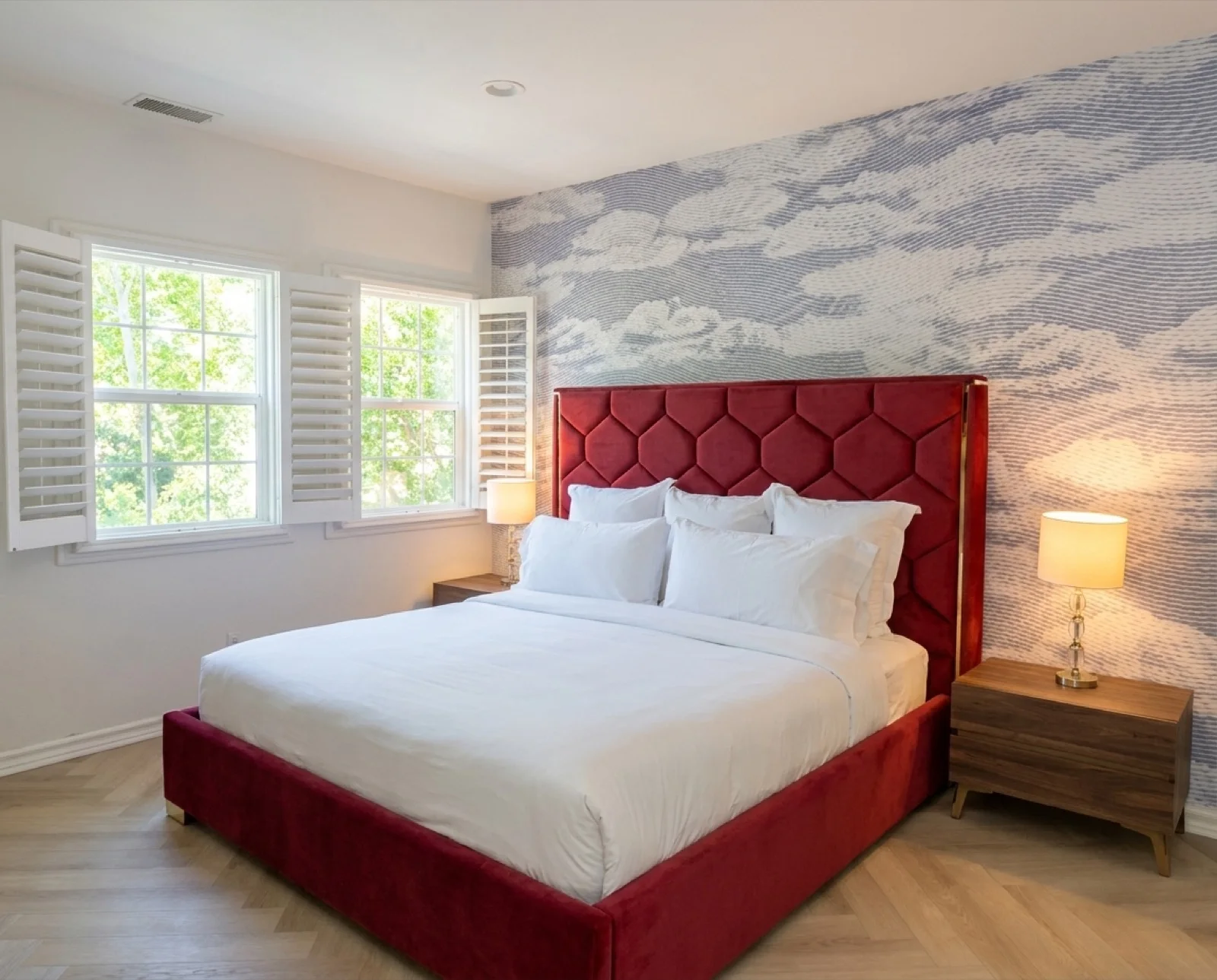 The Ruby Room: a private bedroom with a deep red velvet honeycomb headboard and soft cloud-mural wallpaper