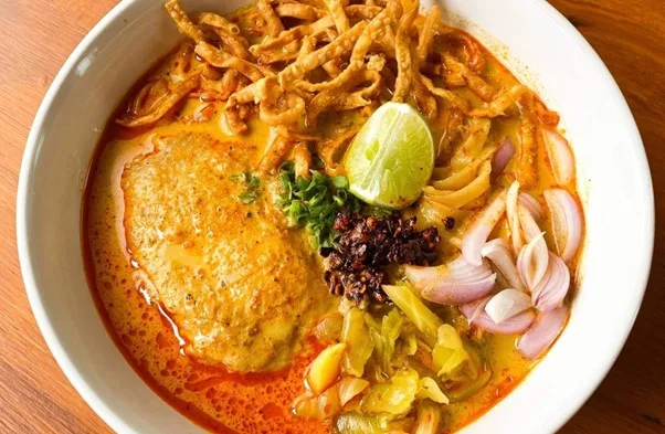 A bowl of khao soi topped with crispy noodles, lime, and shallots