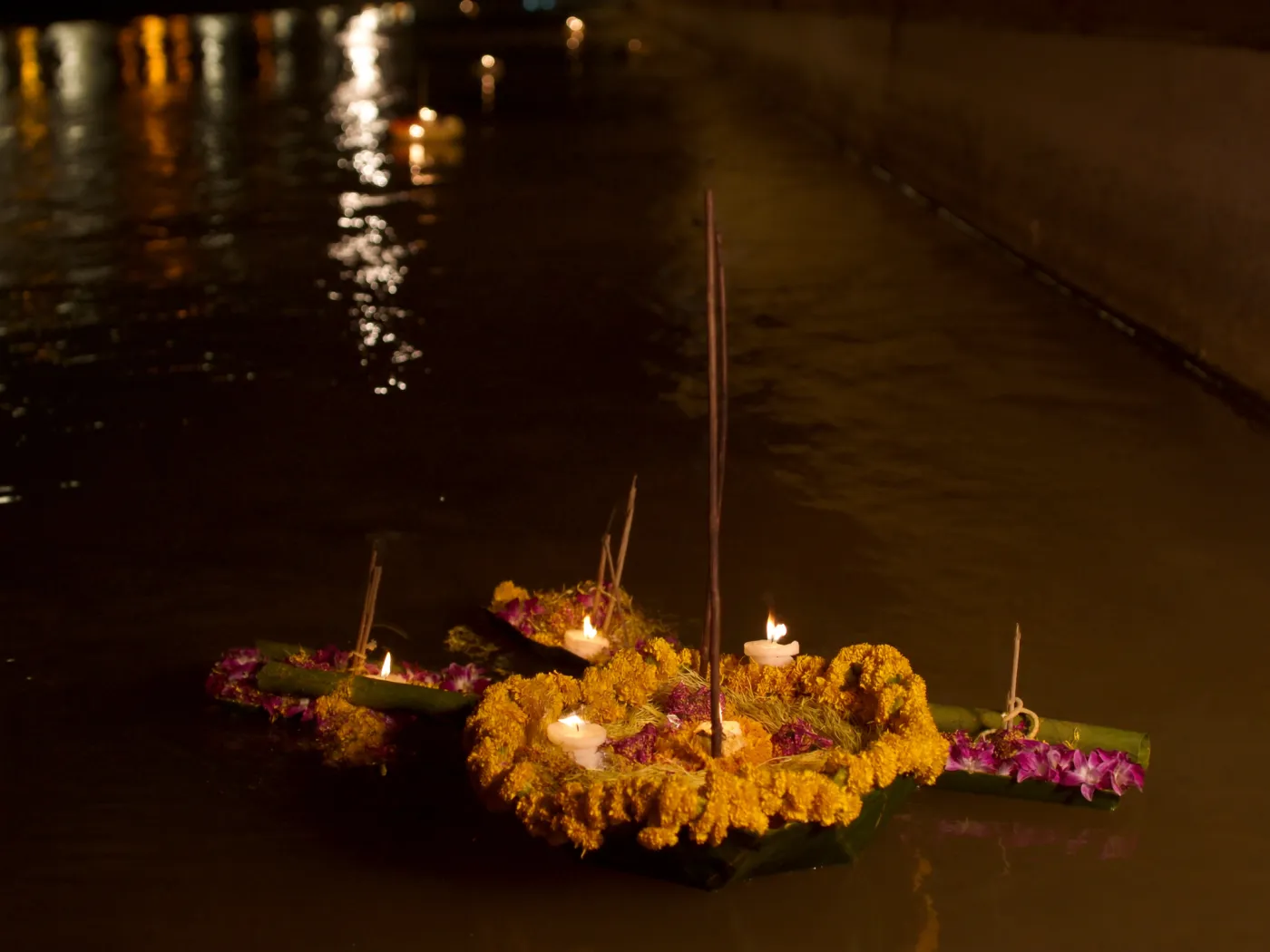 Candlelit krathongs of marigolds and orchids floating on dark water