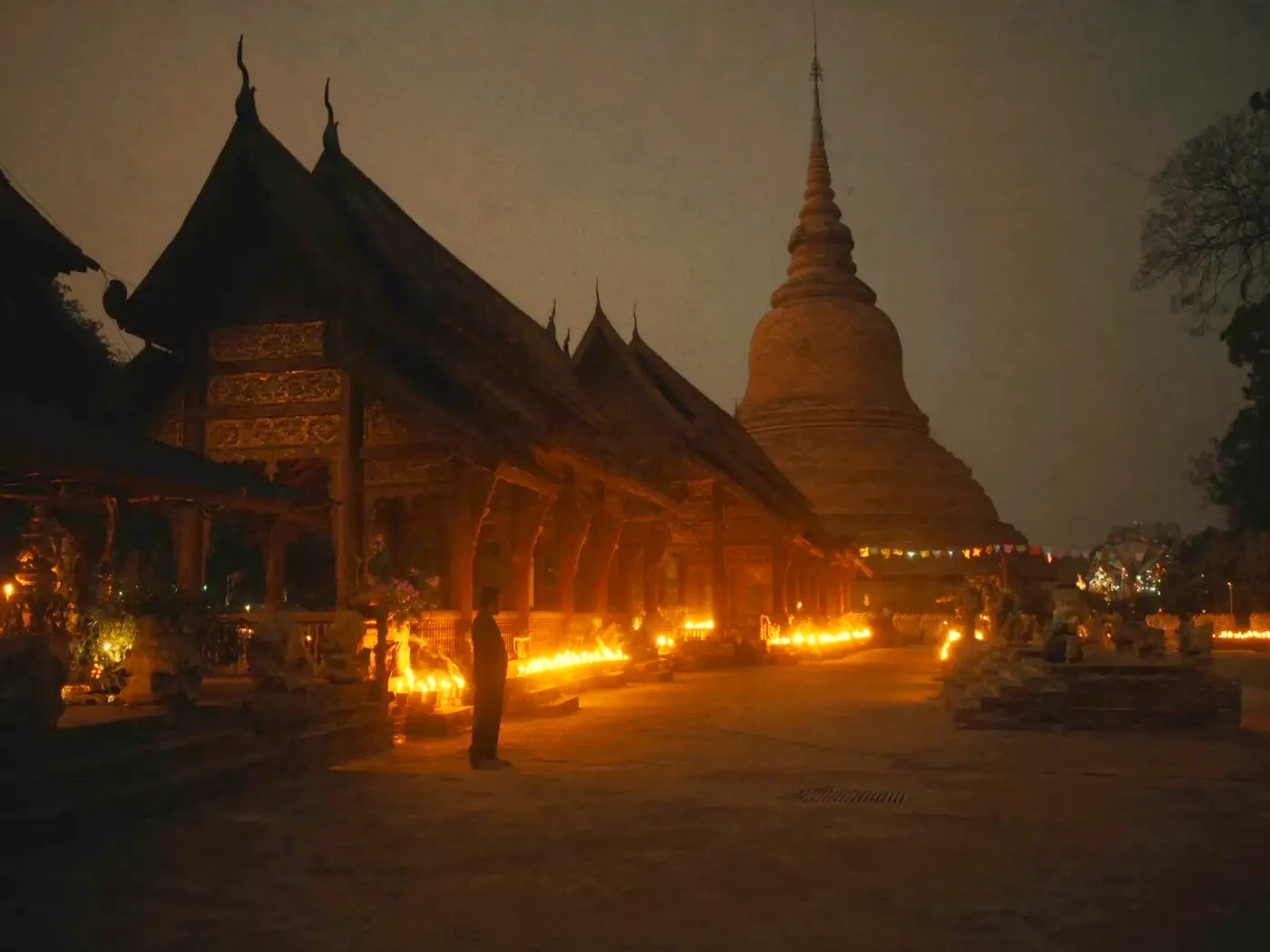 Candle offerings glowing along an Old City temple walk, the golden chedi rising behind, the evening Buddhist Lent begins