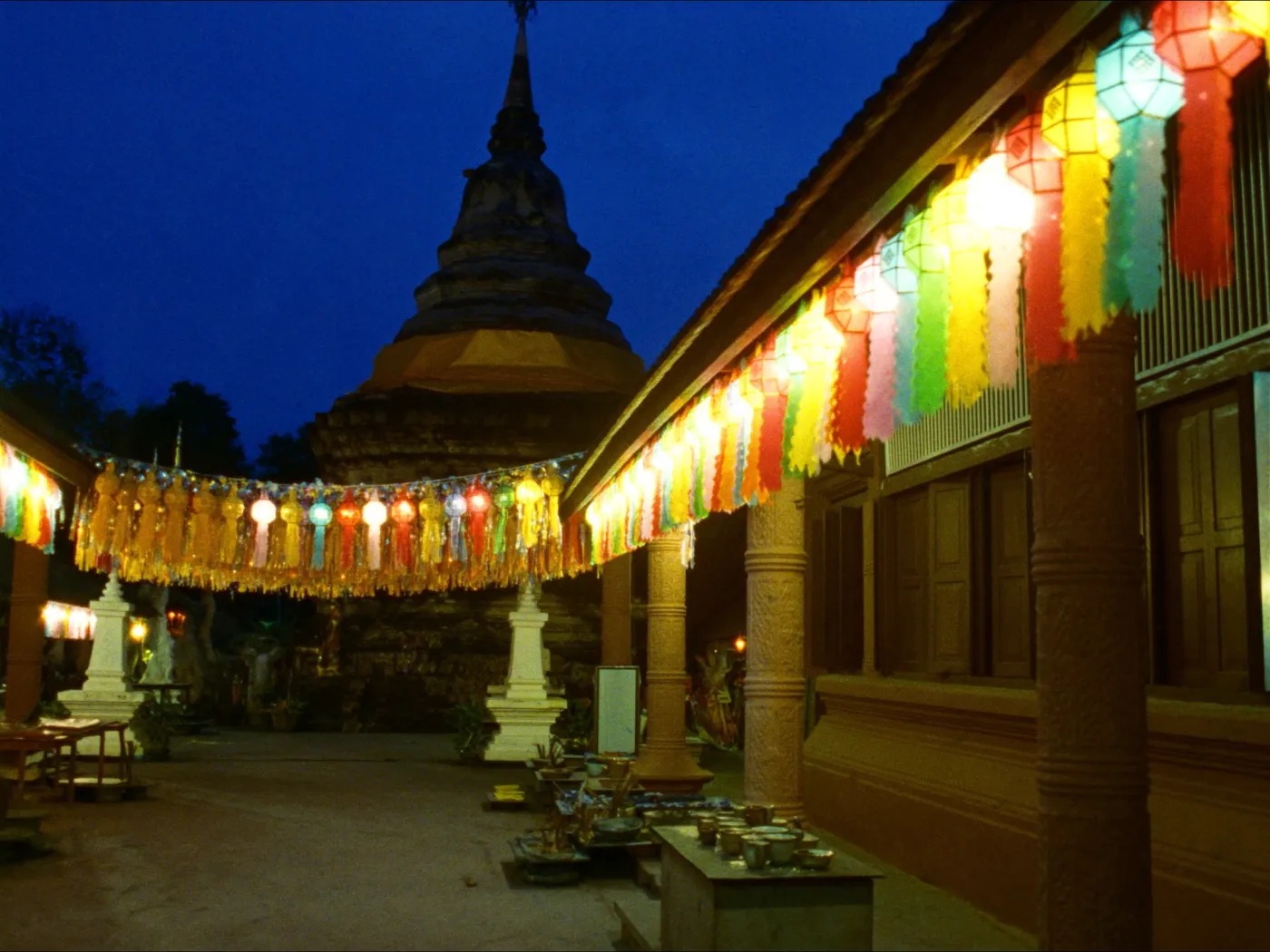 Colorful Lanna lanterns strung across a temple courtyard at dusk