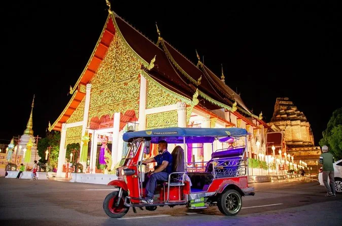 A red tuk-tuk passing an ornate temple at night